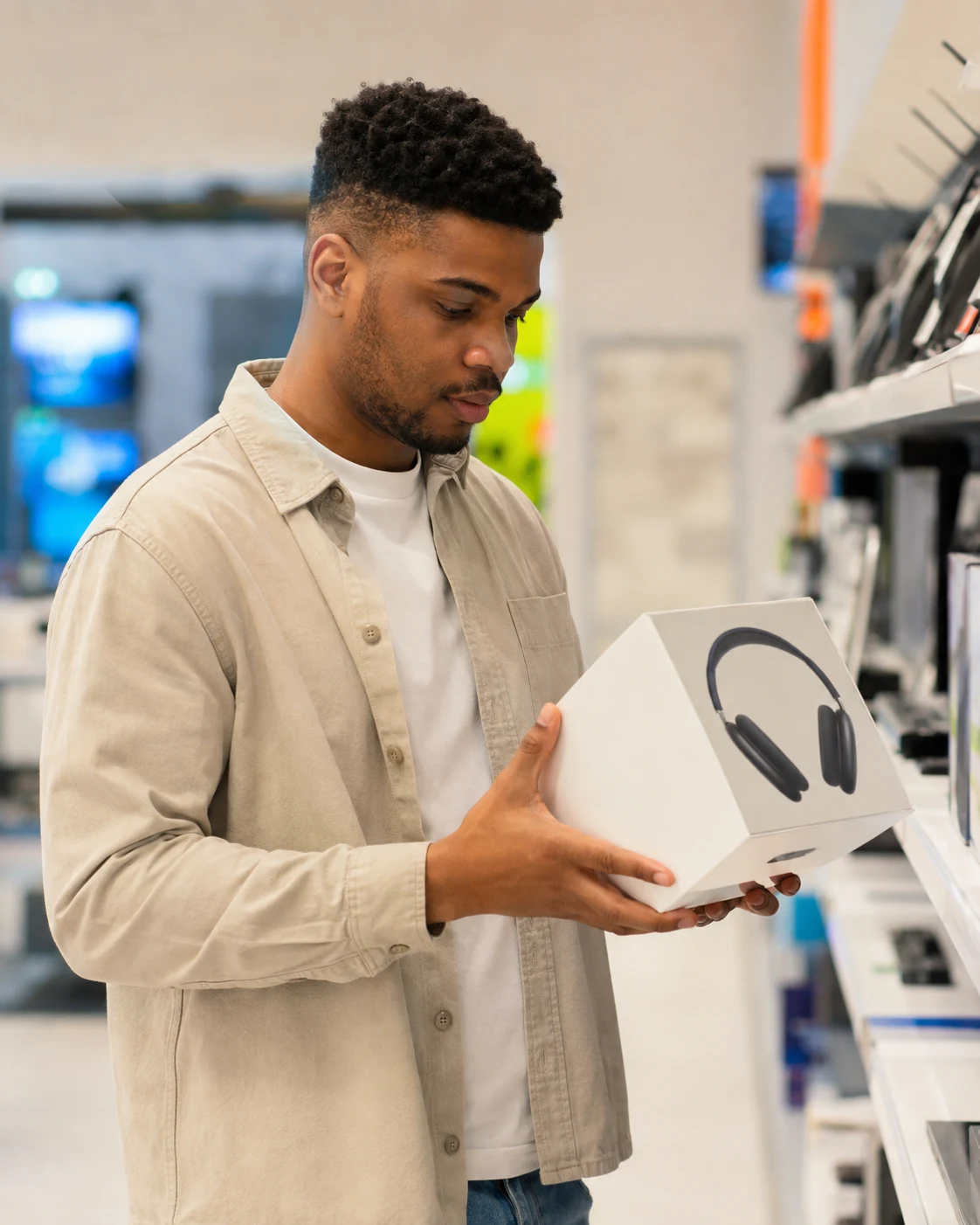 An electronics shopper holding a boxed pair of headphones in a store